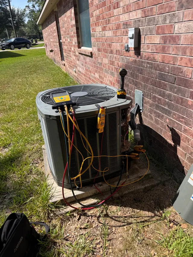 Technician tools and gauges set up beside a condenser at a brick home