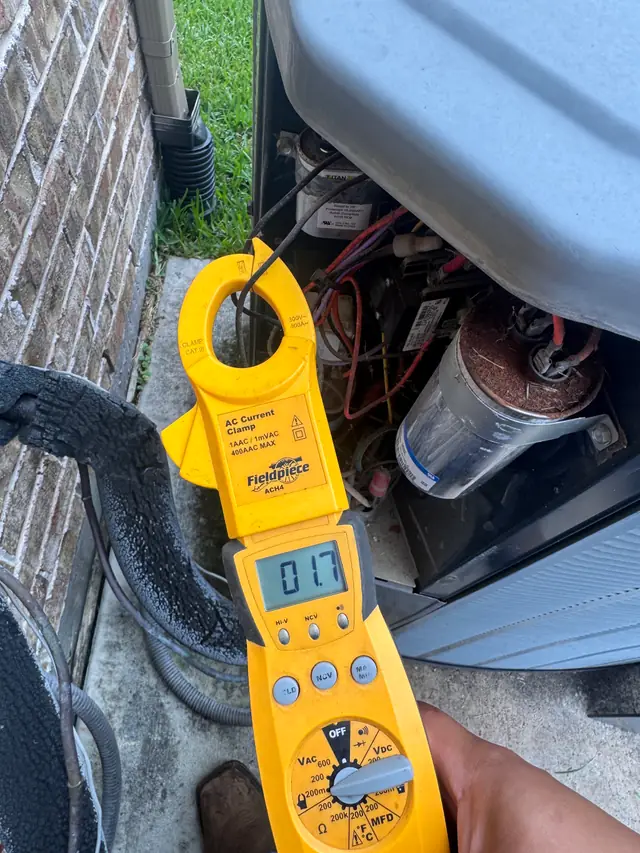 Technician holding a clamp meter reading 01.7 beside an open condenser
